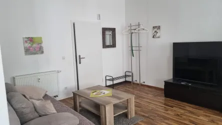 Ein stilvolles Wohnzimmer mit einem gemütlichen Sofa, einem Fernseher und einem Holztisch. Es gibt einen Kleiderständer und Kunstwerke an der Wand.