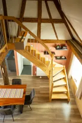 Ein modernes Wohnzimmer mit einer eleganten Holztreppe. Der Raum hat große Fenster und eine warme Farbgestaltung.