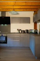 Eine moderne Küche mit grauen Schränken und Edelstahlgeräten. Holzdecke und warmes Licht sorgen für eine einladende Atmosphäre.