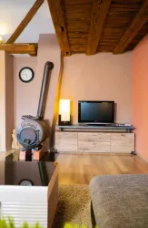 Ein gemütlicher Wohnraum mit Holzdecken, einem Fernseher und einem modernen Kamin. Die Wände sind in warmen Farbtönen gehalten, was eine einladende Atmosphäre schafft.