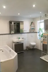 Ein modernes Badezimmer mit einer Badewanne, Dusche und einem Waschbecken. Die Wände sind hell und es gibt Pflanzen für eine entspannende Atmosphäre.