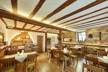 Ein gemütliches Restaurant mit Holzbalken und rustikalem Interieur. Die Tische sind ordentlich gedeckt und schaffen eine einladende Atmosphäre.