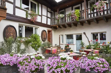 Ein einladender Innenhof mit vielen blühenden Pflanzen und Blumen. Gemütliche Sitzgelegenheiten und Holzdetails verleihen dem Ort eine charmante Atmosphäre.