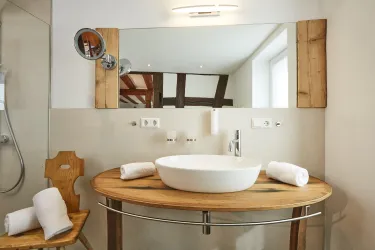 Ein modernes Badezimmer mit einem runden Waschbecken und Holzdetails. Handtücher liegen ordentlich auf dem Tisch und ein großer Spiegel reflektiert den Raum.