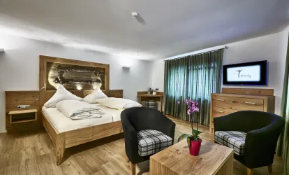 Ein modernes Schlafzimmer mit einem großen Doppelbett und Holzmöbeln. Ein gemütlicher Sitzbereich mit zwei Stühlen und einem Tisch ist ebenfalls vorhanden.