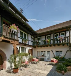 Ein charmanter Innenhof mit traditionellen Fachwerkhäusern. Bunte Blumen und Tische laden zum Verweilen ein.