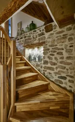 Eine elegante Holztreppe führt zu einem gemütlichen Raum. Die Steinmauer und dekorativen Flaschen verleihen dem Ambiente einen rustikalen Charme.