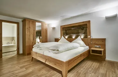 Ein modernes Schlafzimmer mit einem großen Doppelbett aus Holz und gemütlichen Betten. Der Raum hat einen warmen Holzfußboden und eine helle, einladende Atmosphäre.