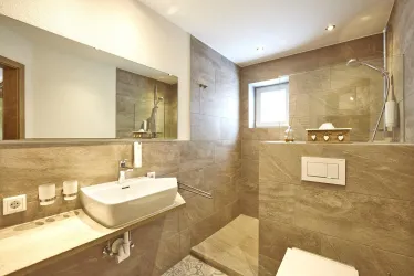 Ein modernes Badezimmer mit keramischen Fliesen und einer Dusche. Es gibt einen großen Spiegel und eine elegante Waschbeckenlösung.