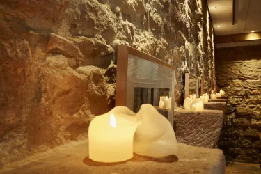 Eine gemütliche Wand aus Naturstein mit mehreren Kerzen und Bildern. Die warmen Lichter sorgen für eine entspannende Atmosphäre.