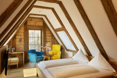 Ein gemütliches Zimmer mit Holzdecken und modernen Möbeln. Es gibt ein großes Bett und farbige Sessel in der Ecke.