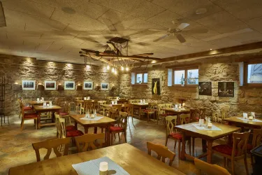 Ein gemütliches Restaurant mit Holzstühlen und rustikalen Steiwänden. Die warmen Lichter schaffen eine einladende Atmosphäre.