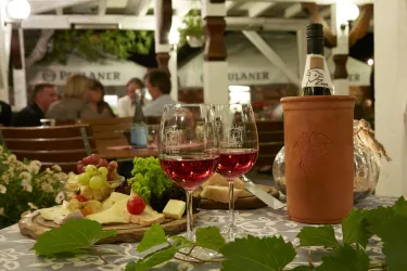 Ein schöner Tisch mit zwei Gläsern Roséwein und einer Flasche in einem Kühler. Im Hintergrund sind andere Gäste zu sehen und eine ansprechende Atmosphäre.