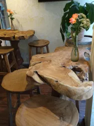 Ein gemütlicher Tisch aus Holz mit einer natürlichen Form steht in einem Raum. Daneben befinden sich Holzhocker und eine Vase mit einer Rose.