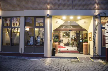 Ein eleganter Eingang zu einem Hotel mit beleuchtetem Dach und großen Fenstern. Die Atmosphäre ist einladend und modern.