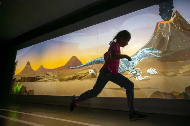 Ein Kind läuft im Wettlauftunnel gegen einen animierten Dinosaurier. Foto: Dynamikum Science Center Pirmasens/Sebastian Fachenbach