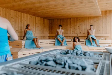 Eine Sauna mit mehreren Menschen, die entspannt auf Bänken sitzen. Die Atmosphäre ist ruhig und einladend.