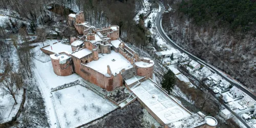 Eine alte Burg, umgeben von schneebedeckten Bäumen und einer ruhigen Landschaft. Die Struktur der Burg hebt sich deutlich von der weißen Schneedecke ab.