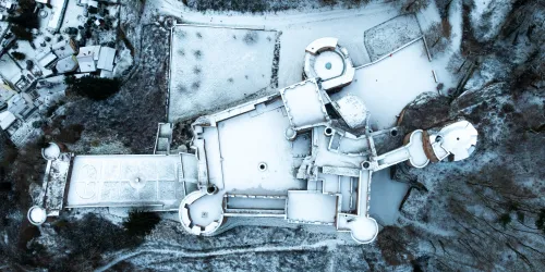 Eine schneebedeckte Burg von oben gesehen. Die Gebäude sind umgeben von einer winterlichen Landschaft.
