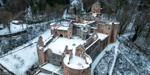 Eine beeindruckende Burgruine im Schnee, umgeben von schneebedeckten Bäumen. Die Architektur zeigt mittelalterliche Merkmale und vermittelt einen geheimnisvollen Eindruck.