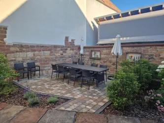 Ein gemütlicher Außenbereich mit einem großen Esstisch und Stühlen. Umgeben von schönen Pflanzen und einer natursteinernen Wand.