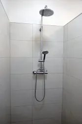 Eine moderne Dusche mit einem großen Regenduschkopf und einem Handbrause. Die Wände sind hell gefliest und vermitteln ein sauberes, minimalistisches Design.