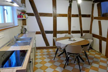 Eine gemütliche Küche mit einem Tisch und Stühlen. Die Wände sind mit Holzbalken versehen und der Boden hat ein kariertes Muster.