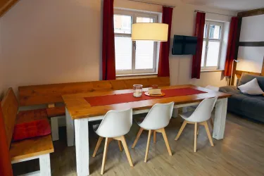 Ein gemütlicher Essbereich mit einem großen Holztisch und Stühlen. Helle Fenster und moderne Einrichtung schaffen eine einladende Atmosphäre.