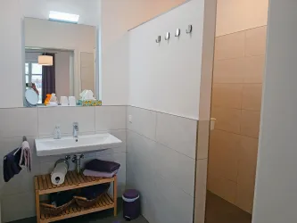 Ein modernes Badezimmer mit einem Waschbecken, Handtüchern und einer Dusche. Es ist hell und schlicht eingerichtet.