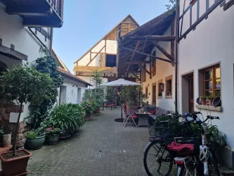 Ein einladender Innenhof mit gemütlichen Sitzgelegenheiten und vielen Pflanzen. Im Hintergrund ist ein traditionelles Gebäude mit einem schönen Dach zu sehen.