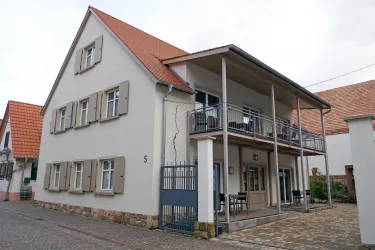 Ein modernes Haus mit einem großen Balkon und mehreren Fenstern. Die Architektur ist freundlich und einladend, ideal für ein Wohn- oder Geschäftsgebäude.