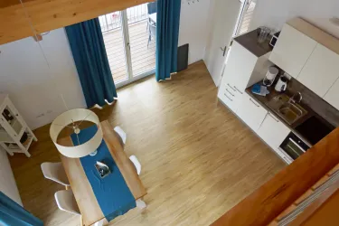 Eine moderne Küche mit einem Essbereich und einem großen Tisch. Große Fenster lassen viel Licht herein und die offenen, blauen Vorhänge schaffen eine einladende Atmosphäre.