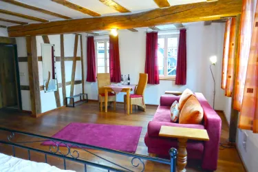 Ein gemütliches Zimmer mit Holzdecken und roten Vorhängen. Es gibt ein Sofa, einen Tisch und einen großen Spiegel.