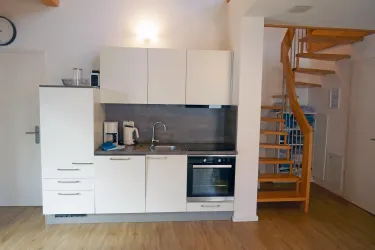 Eine moderne Küche mit weißen Schränken und Edelstahlgeräten. Eine Holztreppe führt nach oben.