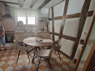 Eine moderne Küche mit einem runden Tisch und vier Stühlen. Die Wände sind teilweise mit Holz verkleidet und es gibt viel natürliches Licht.