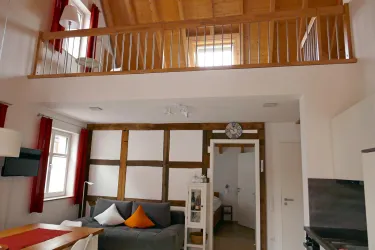 Ein modernes Wohnzimmer mit hohen Decken und offenen Raumkonzept. Im Hintergrund sieht man eine gemütliche Schlafebereich auf einer Galerie.