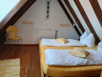 Ein gemütliches Schlafzimmer mit zwei Einzelbetten und gelben Kissen. Die Holzverkleidung und die schräge Decke verleihen dem Raum eine warme Atmosphäre.