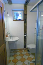 Ein kleines Badezimmer mit Dusche, Waschbecken und Toilette. Die Wände sind in neutralen Farben gehalten und es gibt Fliesen mit einem einfachen Muster.