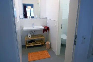 Ein modernes Badezimmer mit einem Waschbecken und einem Handtuchständer. Der Raum ist hell und sauber, mit einem kleinen Teppich auf dem Boden.