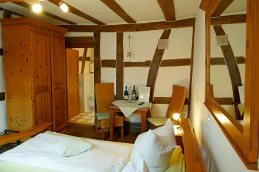 Ein gemütliches Zimmer mit Holzmöbeln und einem Tisch für zwei. Die Wände sind mit sichtbaren Balken gestaltet, was eine einladende Atmosphäre schafft.