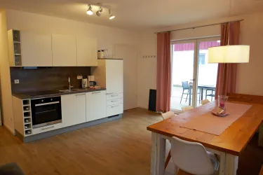 Eine moderne Küchenzeile mit einem Essbereich aus Holz. Es gibt große Fenster, die viel Licht hereinlassen.