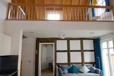 Eine moderne Wohnung mit einem offenen Wohnraum und einer Galerie. Die Wände bestehen aus Holz und weißen Akzenten, und der Raum ist hell und einladend.