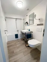 Ein modernes Badezimmer mit einer Badewanne und einem Waschbecken. Die Wände sind hell und die Böden aus Holzoptik.