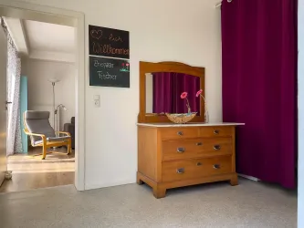 Ein einladender Eingangsbereich mit einem Holzschrank und einer Spiegelfläche. Ein Bereich ist mit lila Vorhängen abgetrennt und ein Willkommensschild hängt an der Wand.