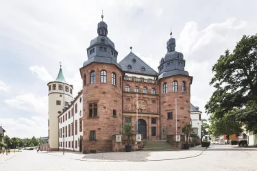 Ein historisches Gebäude mit schönem Fassadendesign und Türmen. Die Architektur zeigt traditionelle Elemente und ist von einem öffentlichen Platz umgeben.