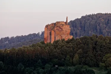 Eine beeindruckende Felsformation ragt über die umgebenden Wälder. Der Himmel ist sanft gefärbt und vermittelt eine ruhige Atmosphäre.
