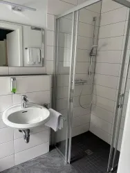 Ein modernes Badezimmer mit einer gläsernen Dusche und einem Waschbecken. Die Wände sind hell gefliest, und es gibt ein Handtuch und Seife bereit.