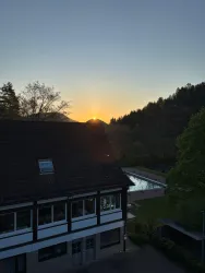 Ein schöner Sonnenuntergang hinter den Bergen. Im Vordergrund sieht man ein Gebäude und einen Pool.
