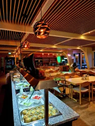 Ein modernes Restaurant mit einem Buffet, das frische Speisen anbietet. Die Einrichtung ist hell und gemütlich, mit stilvollen Lampen und einem einladenden Ambiente.