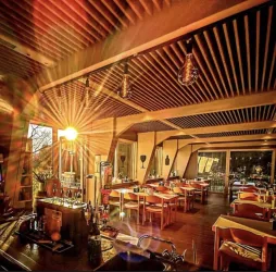 Ein modernes Restaurant mit warmem Licht und einladenden Tischen. Die Sonne strahlt durch große Fenster und schafft eine gemütliche Atmosphäre.